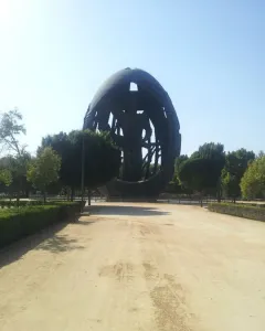 The Birth of a New Man sculpture stands at the end of a dirt path in a park, with trees and bushes around it.