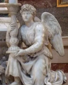 Angel sculpture kneeling and holding an ornate candlestick, with flowing robes and curly hair.