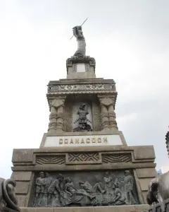 Cuauhtémoc Monument with tiered stone reliefs and a statue holding a spear-like object on top