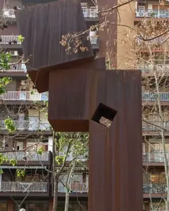 El Llarg Viatge, a tall rust-colored abstract metal sculpture with a square cutout on a brick platform.