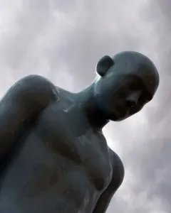 Greetingman sculpture with a bowed head against a cloudy sky.