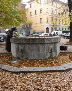 Saint Francis Fountain beside a basin covered with fallen autumn leaves, with a robed statue holding a red rose.