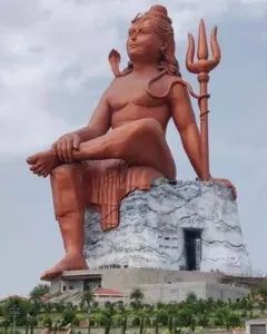 The Statue of Belief, a massive seated Shiva statue with a cobra and trident on a large base under a cloudy sky.