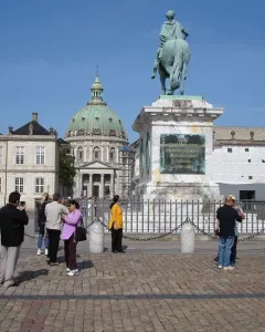 Frederick V equestrian statue on a tall marble pedestal in a sunny square, with people nearby and a green-domed church in the background.