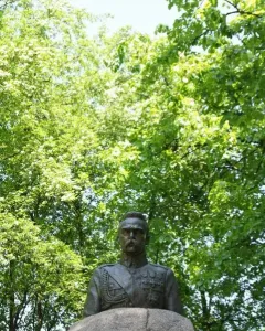 Bronze bust of Józef Piłsudski in military uniform on a rough stone pedestal with an inscription plaque.