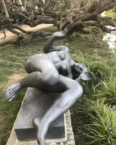 The River, a dark reclining nude female sculpture on a stone plinth outdoors.