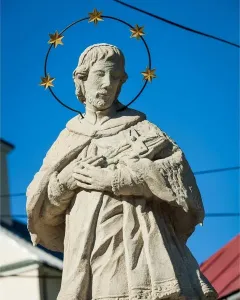 Sandstone statue of St. John of Nepomuk with a halo of stars against a blue sky.