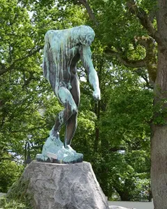 The Shade bronze sculpture of a nude male figure leaning forward on a rock in a garden setting.