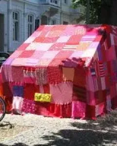Ruhender Verkehr, a vehicle covered in a colorful knitted textile blanket on a city street.