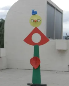 The Caress of a Bird sculpture with stacked colorful abstract shapes on a green pillar.