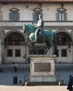 Ferdinando I de\' Medici equestrian statue on a stone pedestal in a public square with a historic building behind it.