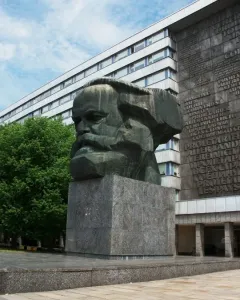 Karl Marx Monument, a large dark bust on a tall granite pedestal, with a modern building behind it.