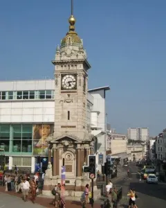 Brighton Clock Tower standing in a busy city plaza with pedestrians, a red double-decker bus, and a street beside it.