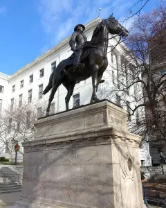 Joseph Hooker equestrian statue on a tall stone pedestal with HOOKER inscribed on the base, set against buildings and blooming trees.
