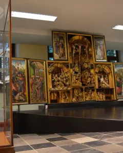 The Fisenne Altarpiece with gilded sculptural reliefs and painted side panels on a dark display stand.