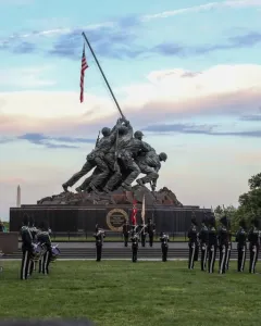 The Marine Corps War Memorial at twilight, with a military band or honor guard assembled on the lawn in front of the statue.