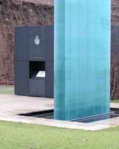 The National Police Memorial with a tall translucent teal column beside a dark memorial structure.