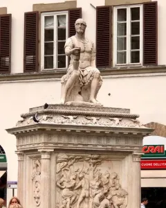 Giovanni delle Bande Nere statue on an ornate pedestal in a busy square with bicycles and pedestrians nearby.