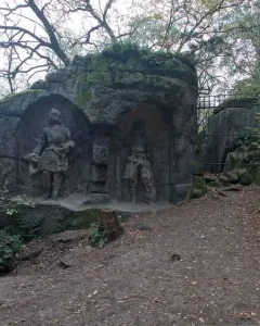 Klácelka stone reliefs in a wooded setting, with carved figures in recessed niches and iron gates in front.