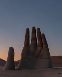 Mano del Desierto rising from a barren desert landscape at dusk with distant mountains on the horizon.