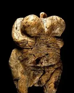 Venus of Hohle Fels figurine with pronounced breasts, rounded abdomen, and a loop-like top against a dark background.
