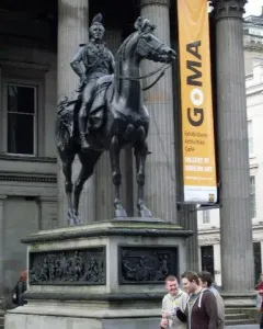 The Duke of Wellington equestrian statue with a traffic cone on its head, standing before a columned building with a GoMA banner.