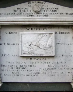Titanic Musicians\' Memorial plaque with a central mourning figure and engraved names on a brick wall.