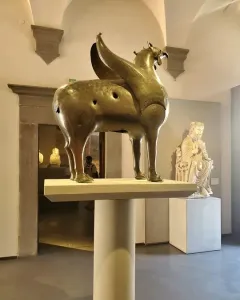 Bronze Pisa Griffin statue on a pedestal in a museum gallery.