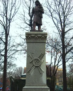 Firemen\'s Monument showing a bronze rescue worker holding a child and lantern atop a tall granite pillar.