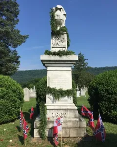 Confederate Memorial stone monument with an urn on top, garlands, and small Confederate flags around the base.
