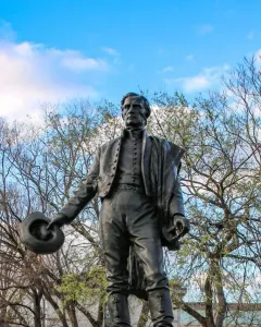 Bronze statue of General José Gervasio Artigas standing outdoors with a hat in his left hand.