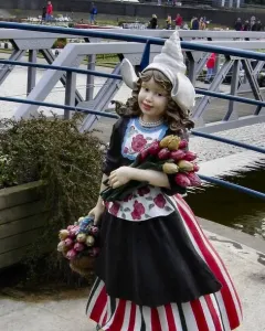Madurodam statue of a Dutch girl in traditional dress holding tulips and wearing clogs beside the water.