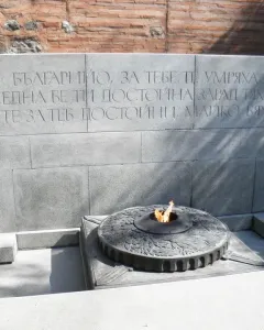 The Unknown Soldier Monument with a grey stone wall, Cyrillic inscription, and an eternal flame in a dark metal basin.