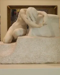 Desolation, a white marble sculpture of a nude kneeling figure with bowed head and long hair draped over the face.
