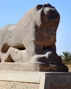 The Lion of Babylon stone sculpture resting on a base beneath a clear blue sky.