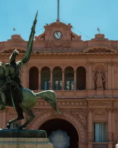 Manuel Belgrano equestrian monument in front of a pink building with arched windows and a central clock.
