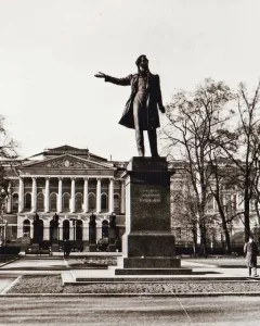 Pushkin statue stands before the Mikhailovsky Palace with a classical facade and trees in the background.