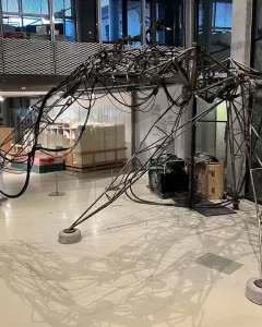 The Senster sculpture with an arched skeletal metal frame, three legs, and cables draped across its structure.