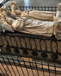 The Tomb of Francis II of Brittany with two recumbent crowned effigies, surrounded by carved figures and enclosed by a black metal fence.