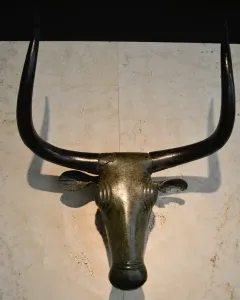 Toros de Costitx bronze bull head sculpture with curved horns and stylized features against a light wall.