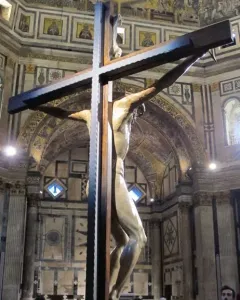 Brunelleschi Crucifix displayed in a decorated church interior with visitors gathered below.