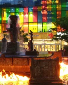 La Joute bronze fountain with water cascading from the center and flames burning on the surrounding pool.