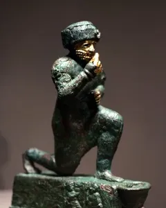 Worshipper of Larsa kneeling figure with a raised hand and gold details on an oxidized green surface.