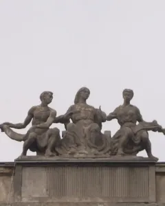 Music sculpture with three seated figures on a rooftop in Warsaw, including a central woman with outstretched hands and a woman holding a stringed instrument.