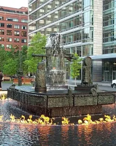 La Joute bronze fountain with water cascading from the center and flames burning on the surrounding pool.