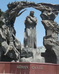 Huseyn Javid monument with a central robed figure, flanked by tall sculptural forms and arching figures above a red stone base.