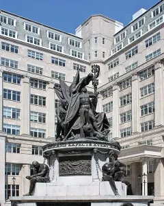 Nelson Monument in Liverpool with bronze figures on a stone base beside a tall stone building.