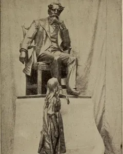 Dickens and Little Nell sculpture showing a seated bearded man and a standing girl looking up at him.
