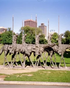 The Partisans sculpture shows several gaunt figures riding skeletal horses and holding tall poles in a grassy urban park.