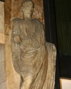 Scior Carera, a weathered stone statue of a draped standing man holding a spherical object, on an inscribed plinth.